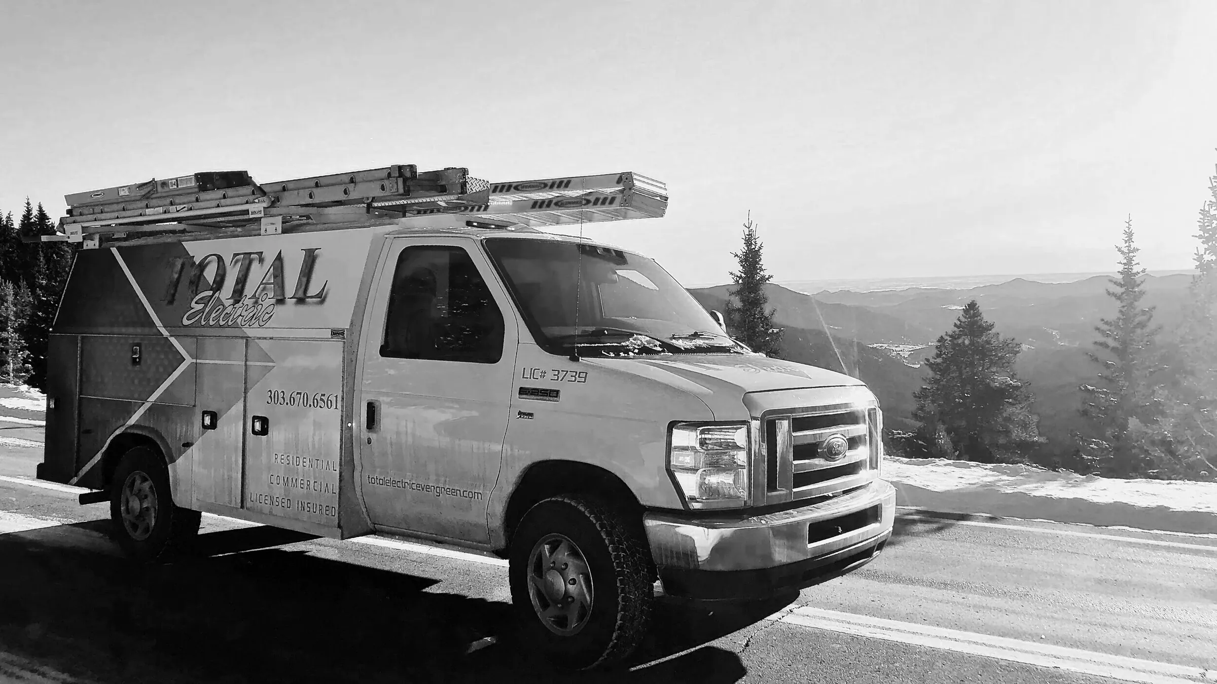 Total Electric service van with ladders on the roof, parked on a mountain road above the foothills