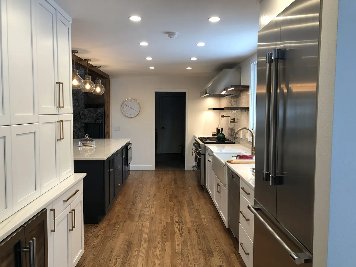 Long white galley kitchen with recessed lights and a stainless fridge
