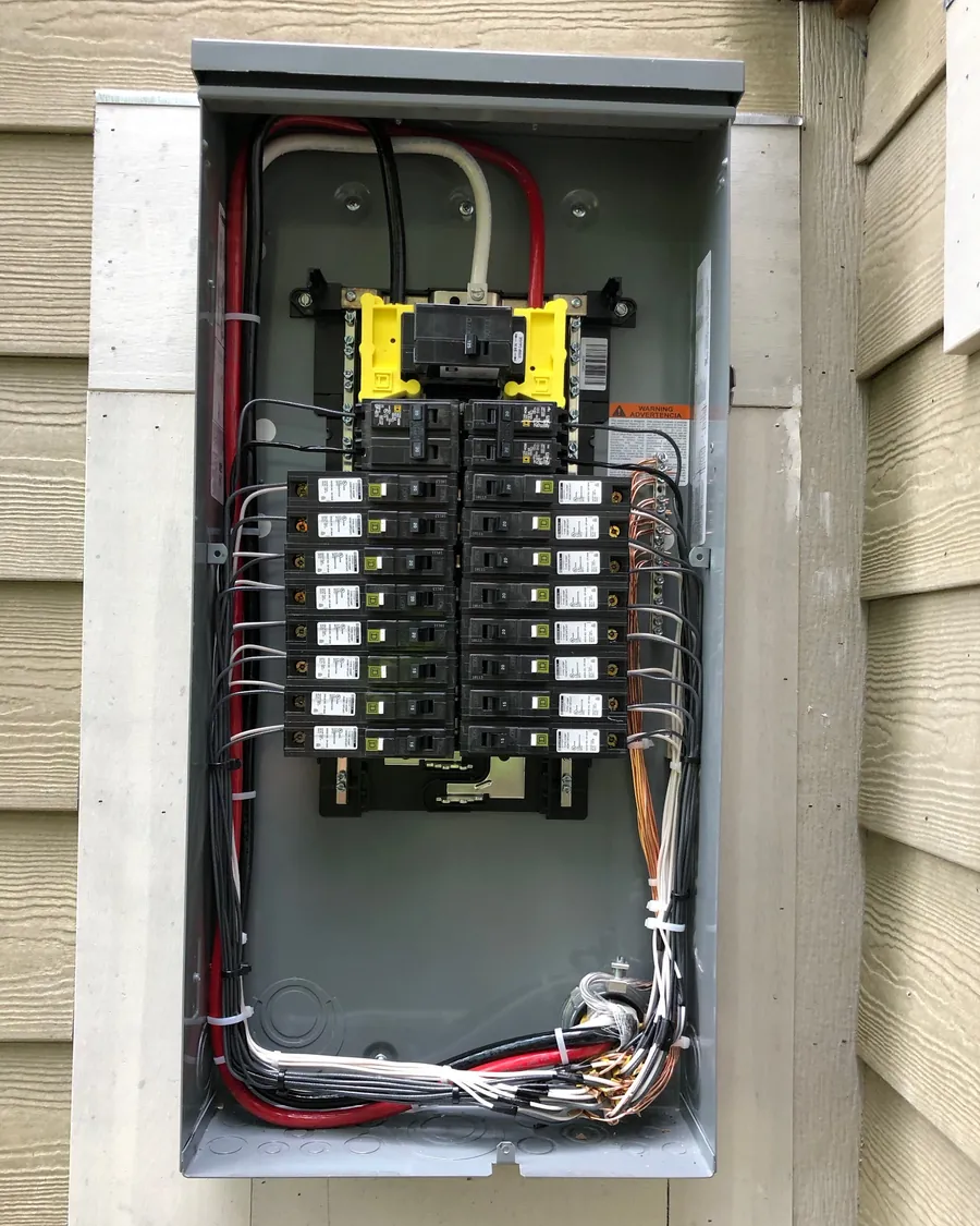 Breaker panel recessed into exterior siding with breakers and wiring visible