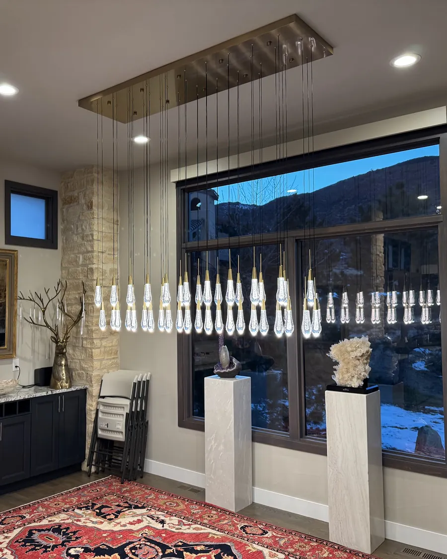 Long crystal pendant with dozens of glass drops hanging in front of a dusk window that looks out at the foothills