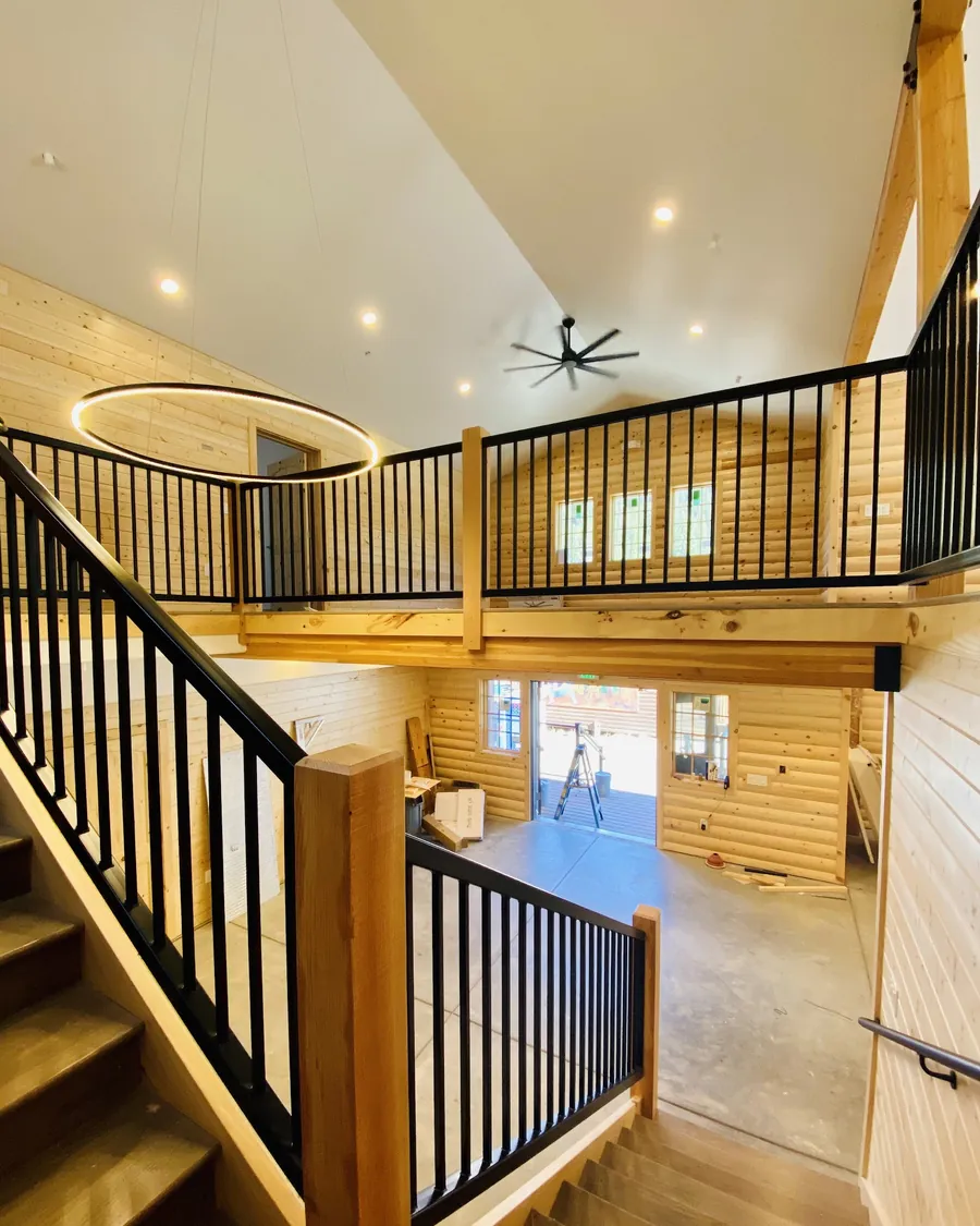 Log home loft with a black railing and a large round LED ring fixture overhead