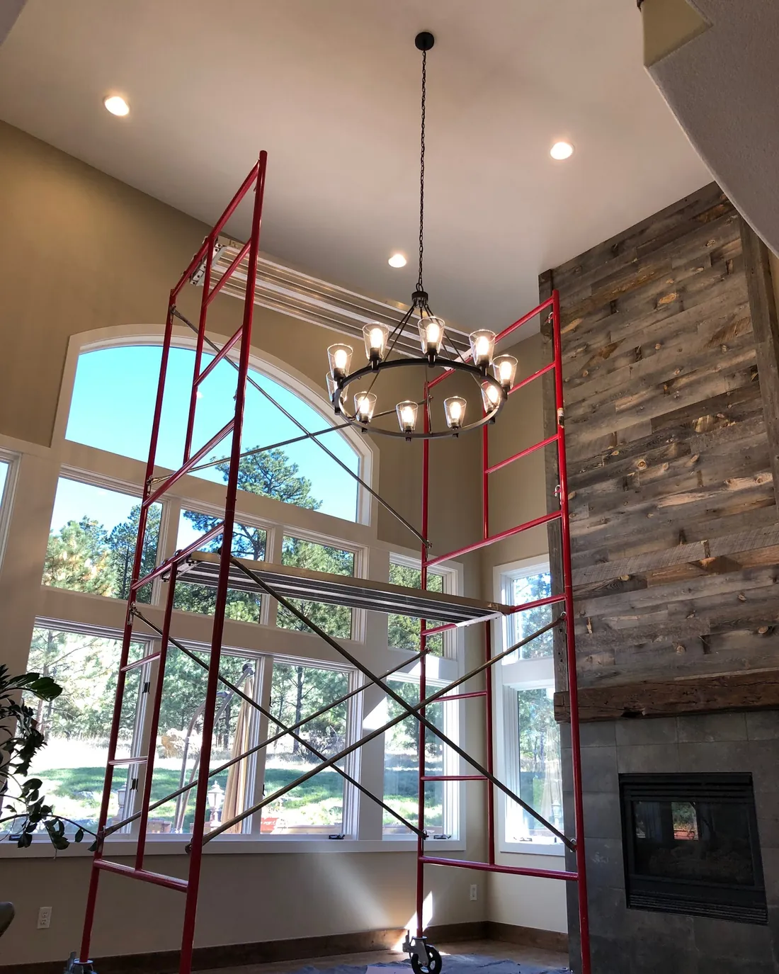 A new iron chandelier hanging in a two-story room, with red rolling scaffold beside it and a fireplace below
